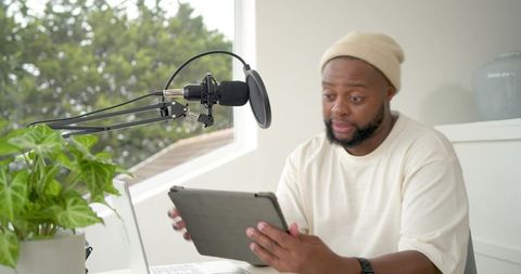 African american creator recording podcast at home studio using tablet and professional mic