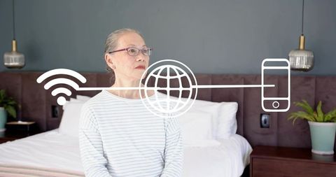 Senior chinese woman sitting on bed wearing glasses and striped top showing wi-fi overlay
