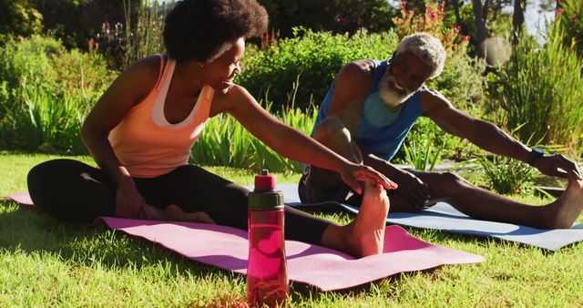 African american senior couple exercising outdoors sitting stretching in sunny garden. staying at home in isolation during quarantine lockdown.