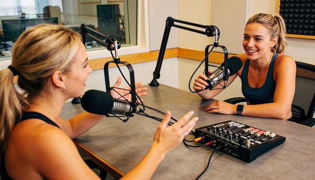 Smiling cohosts recording podcast in professional studio conversing over microphones