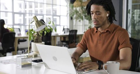 African American Man Working on Laptop in Bright Coworking Space Wearing Earbuds