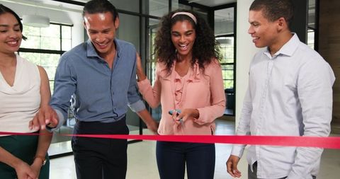 Diverse team cutting ribbon for office celebration