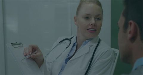 Female doctor explaining diagnosis to patient during clinical consultation with clipboard