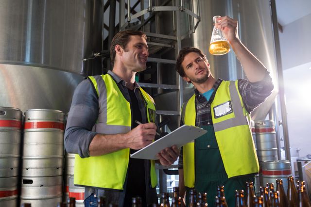 Coworkers examining beer in beaker at warehouse