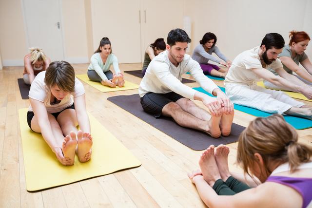 Group of people practicing pashimottanasana in a yoga class, focusing on stretching and flexibility. Ideal for use in content related to fitness, wellness, yoga classes, group exercises, and healthy lifestyles.