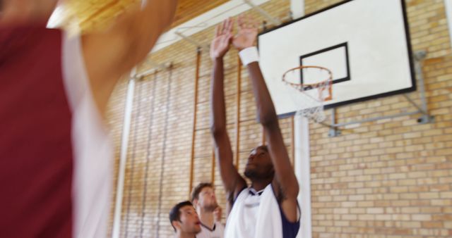 Athletes are actively participating in an intense basketball game inside a gymnasium. Picture captures both offensive and defensive plays near the basketball hoop. Useful for promoting sports events, college athletic programs, or fitness and teamwork themes.