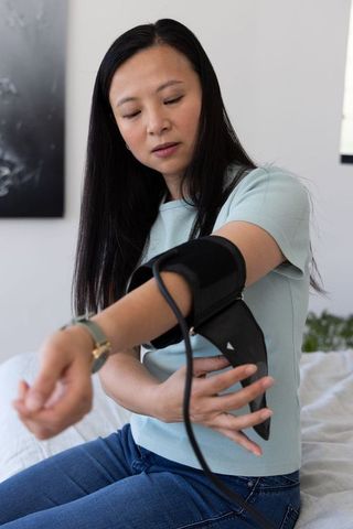 Woman checking blood pressure at home with arm cuff monitor, wellness routine
