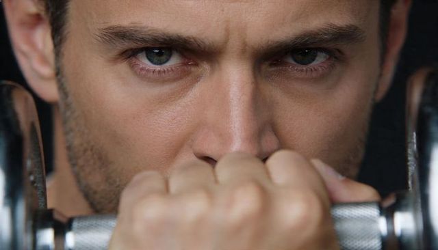 Intense close-up of male gripping knurled dumbbell bar showing determination and grip