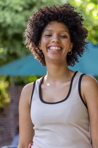 Sunlit african american woman smiling on patio wearing ribbed tank and hoop earrings