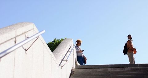 Diverse pedestrians on stone stairs using smartphone and holding basketball with backpack