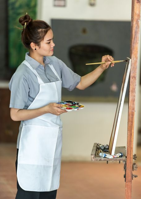 Female artist painting on canvas in studio. Useful for content about creativity, artistic expression, and art-related workshops or classes. Ideal for illustrating themes of skill development, personal hobby or professional artist at work.