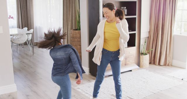 Mother and daughter enjoying quality time dancing together in the living room at home, smiling and having fun. Perfect for use in family-oriented advertising, parenting blogs, lifestyle content, or home decor materials focusing on everyday joy and connection.