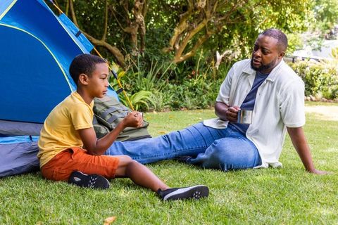 Father and son relaxing in backyard tent sharing coffee and conversation on sunlit lawn