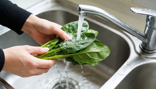 Hands washing fresh spinach under running kitchen faucet for healthy food prep