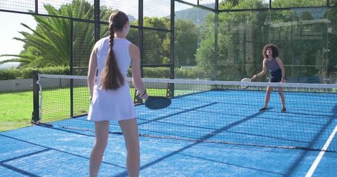 Women playing padel on vibrant blue court with net, outdoor fitness and active lifestyle