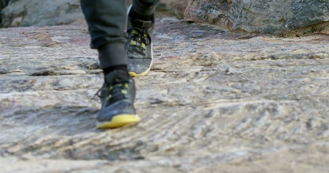 Feet of male rock climber wearing black shoes and walking on rock. Rock climbing, sport, hobbies, healthy lifestyle and outdoor activities, unaltered.