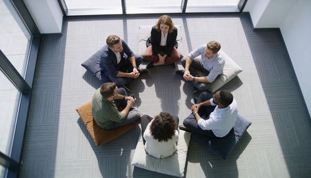 Diverse team holding circle discussion on floor cushions in bright modern office space