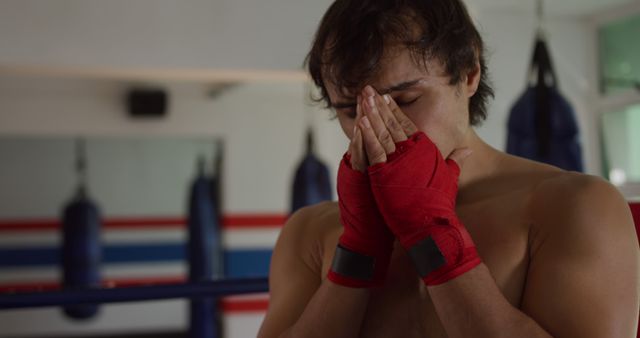 Tired fit caucasian male boxer hiding face in hands in boxing ring. Boxing, sport, strength, training, fitness and competition, unaltered.