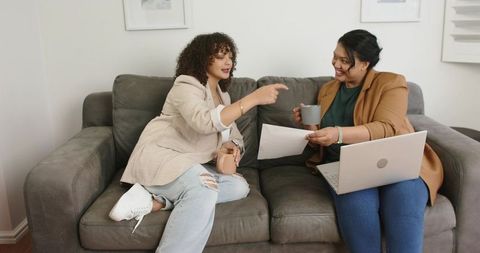 Women Collaborating on Couch Sharing Documents and Laptop Over Coffee for Casual Meeting