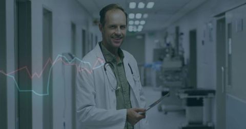 Smiling Male Doctor with Tablet in Hospital Corridor