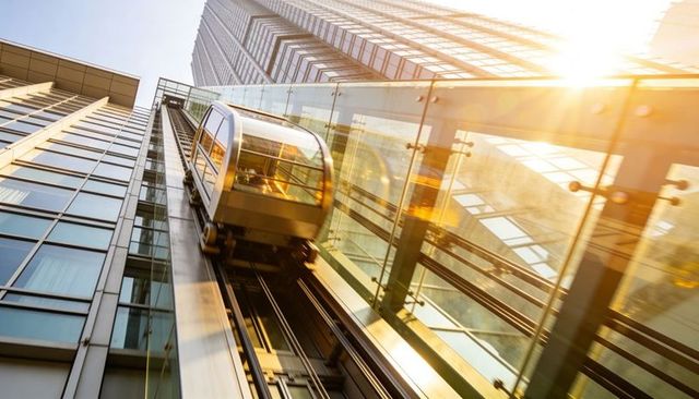 Gliding glass elevator ascending skyscraper facade with reflections and sun flare