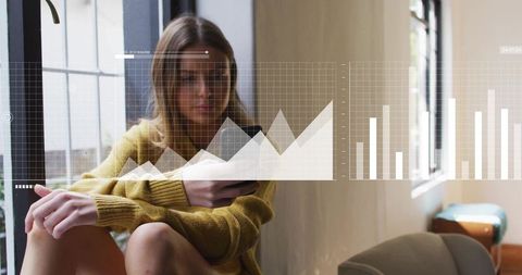 Young woman using smartphone by window with overlaid analytics charts and graphs