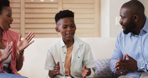 African American parents clapping and cheering son on sofa celebrating joyful family bonding