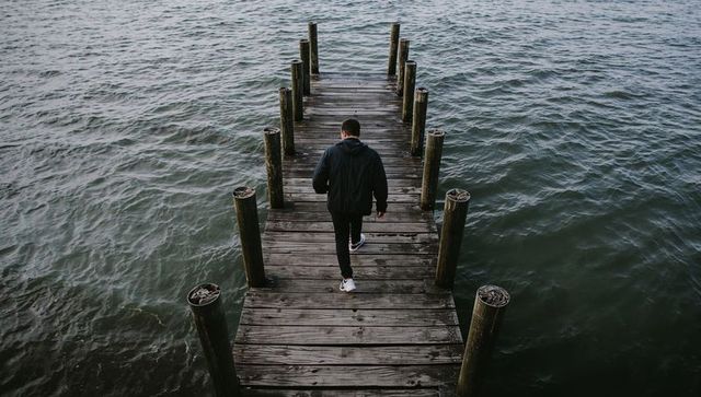 Walking alone on weathered wooden pier over moody sea with pilings and coiled rope