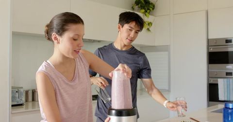 Couple blending pink smoothie in modern minimalist kitchen for healthy morning routine