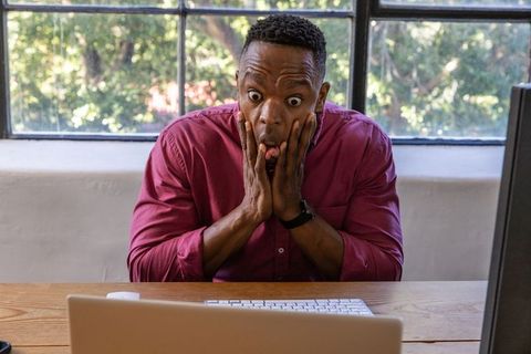 Shocked African American Man at Home Desk with Laptop