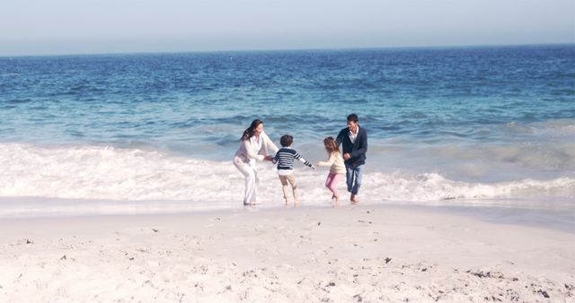 A joyful family is spending time together on a sandy beach. The parents are playing with their two children near the water's edge, creating happy memories. Ideal for themes of family bonding, travel, summer vacations, outdoor activities, and lifestyle.