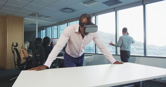 African american businessman using vr headset, with colleagues using computers at office. Business, work and communication.