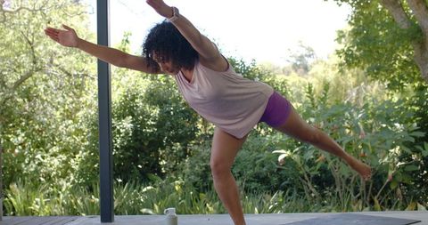 Woman of african descent balancing on one leg practicing outdoor yoga on porch