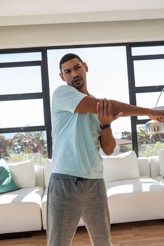 Mid adult man stretching shoulder in modern living room