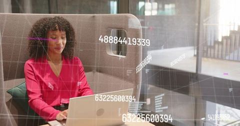 Professional woman in red blouse working on laptop in office booth with data hud overlay