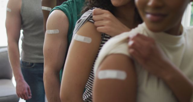 Diverse group of adults standing in line showing bandages on their arms from recent vaccinations. Celebrating community health, unity, and teamwork. Ideal for topics on vaccination campaigns, healthcare awareness, public health initiatives, and medical promotions.