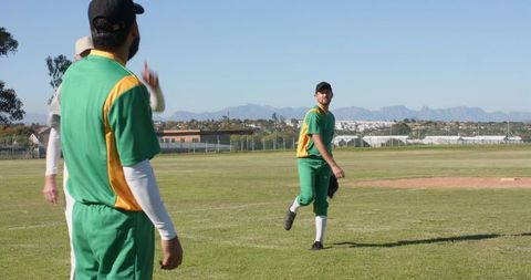 Teammates watching pitcher throwing on sunny baseball field with mountain backdrop