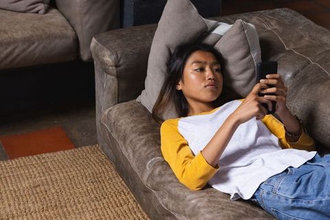 Teenage Girl Relaxing on Sofa Using Smartphone at Home