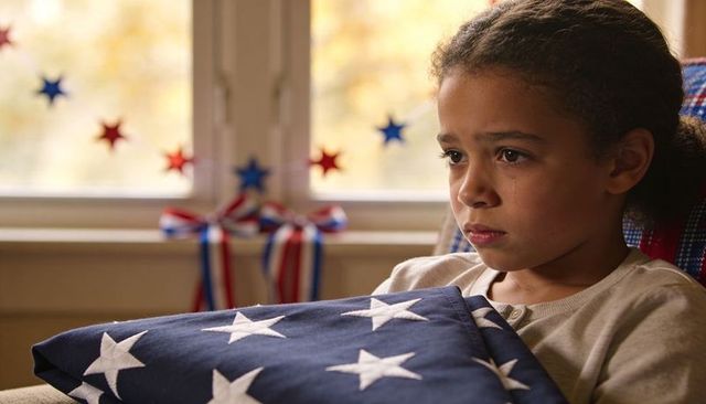 Young girl clutching folded american flag by window, solemn memorial day remembrance