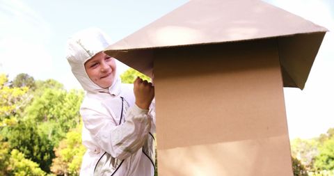 Child in astronaut costume playing with cardboard spaceship outdoors