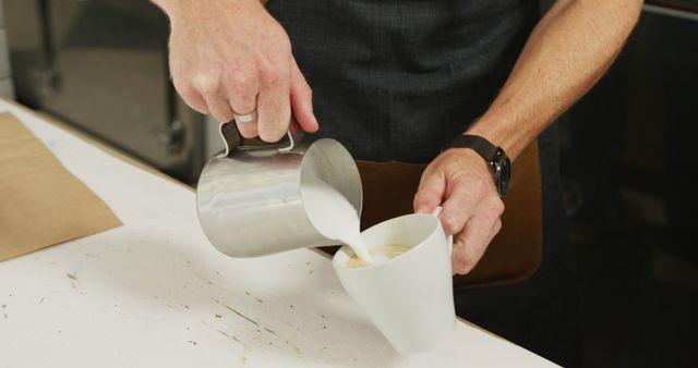 Barista's hands preparing latte art by pouring frothy milk into a freshly brewed cup of coffee. Ideal for depicting coffee culture, cafe atmosphere, or promotional material for coffee shops and barista training programs.