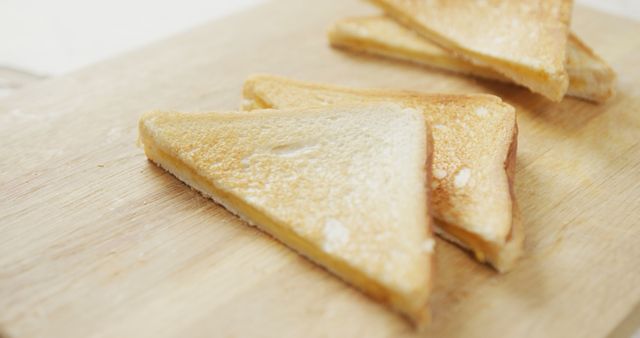 Close-up image of toasted bread slices arranged on a wooden cutting board. Ideal for illustrating concepts related to breakfast, home cooking, simplicity in meals, or kitchen settings. Perfect for use in food blogs, cookbooks, kitchen product advertisements, or healthy eating campaigns.