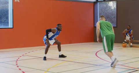 Guarding opponent and defending dribble on indoor basketball court with sunlit orange wall