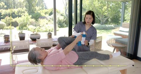 Senior woman receiving assisted resistance band leg exercise on patio rehab table