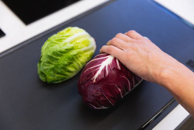 Mid section of male chef cooking in a modern busy kitchen, holding red cabbage on chopping board. Cookery class at a restaurant kitchen. Workshop cooking food.