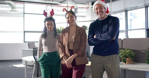 Diverse team celebrating holiday in modern office wearing Santa hat and reindeer antlers