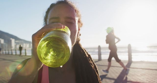 African american woman in sportswear drinking water on promenade by the sea. fitness and healthy outdoor lifestyle.