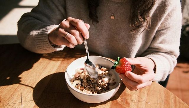 Cozy morning breakfast scooping granola with spoon holding fresh strawberry on wooden table