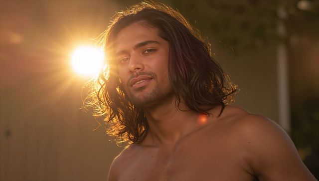 Bare-chested man soaking up golden-hour sunlight with long hair and cinematic lens flare
