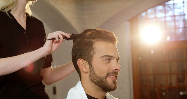 A young Caucasian man is getting his hair styled by a hairstylist, with copy space. Captured in a salon setting, the image reflects a moment of grooming and personal care.